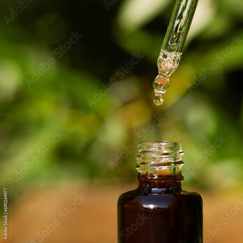 Fototapeta Naklejka Na Ścianę i Meble -  Serum. Close up glass brown bottle with a dropper against green plants blurred background. Skincare detox cosmetics. Skin hydration and moisturising. Essential spa oil. Aroma therapy