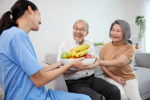 nurse or caregiver serving fruits in a big bowl to senior couple on sofa
