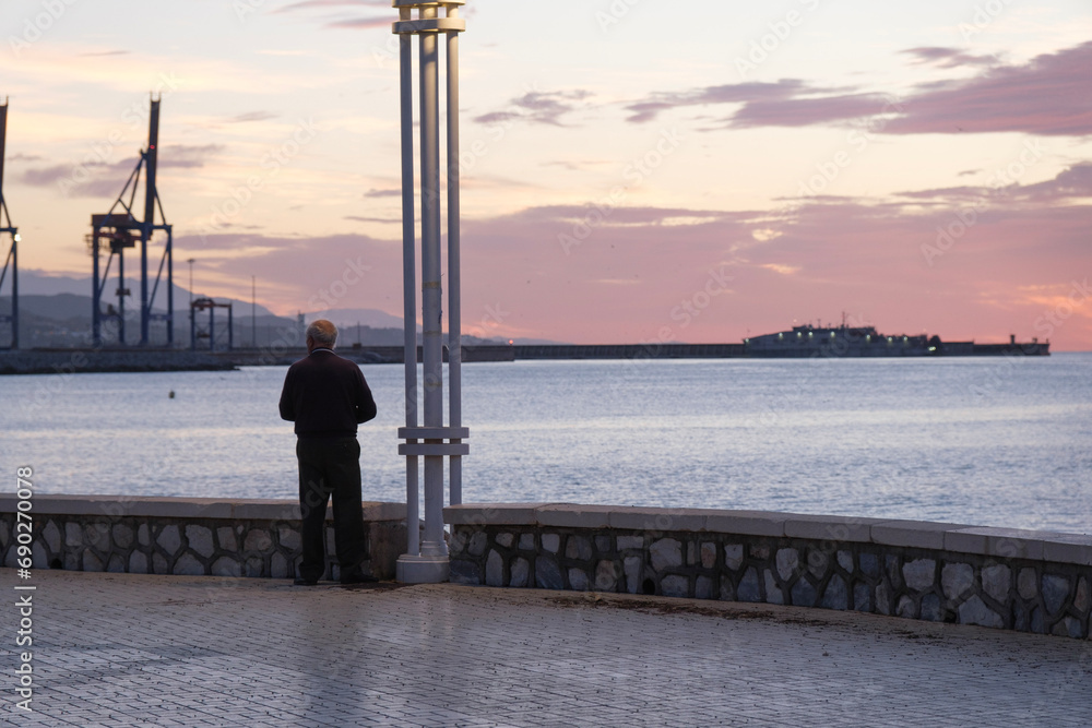 Paseo marítmo de Málaga, amanecer sobre el mar, hombre tercera edad visto de espaldas, mirando los primeros rayos de sol, vida saludable, tranquilidad, soledad