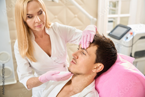 Woman cosmetologist examines the patients face