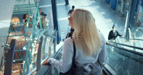 Woman ride down escalator. Back rear view. Woman at airport or train station goes down escalator, looking around. Female traveler tourist arriving by plane in new city town country. Tracking shot