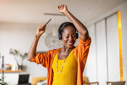 Woman listening to music with headphones connected to her smartphone in the living room at home 