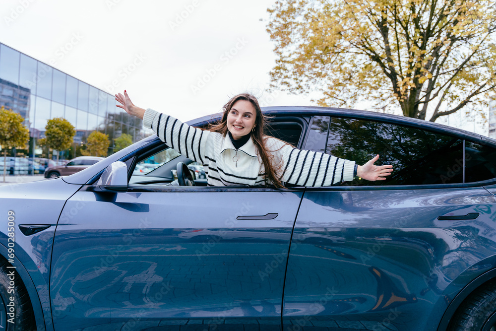 Photo portrait smiling woman enjoying beautiful day wearing striped sweater in car looking out the car window with raised hands on city street outdoor.