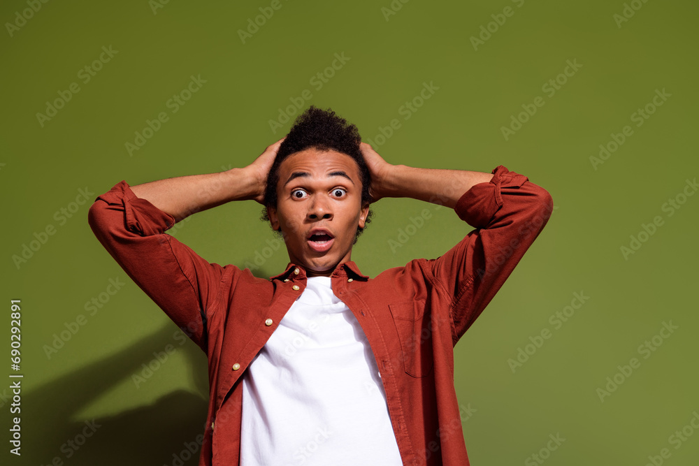 Photo of speechless man with afro hair dressed brown shirt hold hands on head astonished staring isolated on khaki color background Photo of speechless man with afro hair dressed brown shirt hold hands on head astonished staring isolated on khaki color background
