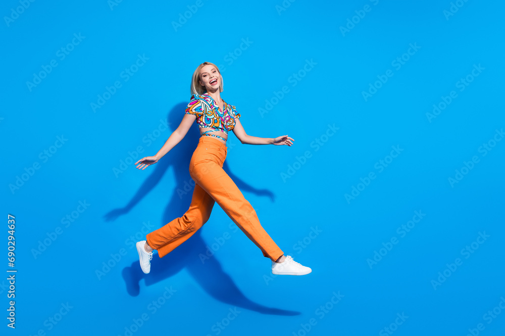 Full size photo of good mood cute girl wear blouse orange trousers run on season sale in empty space isolated on blue color background