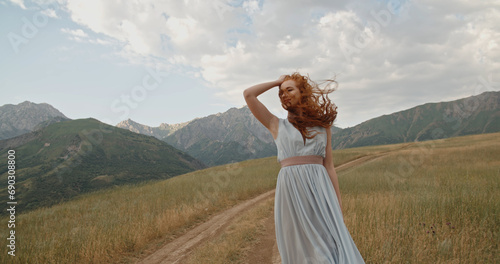 Happy young woman on the mountain road on the sunset or sunrise in summer nature. Pretty young ginger girl in field at sunset. 