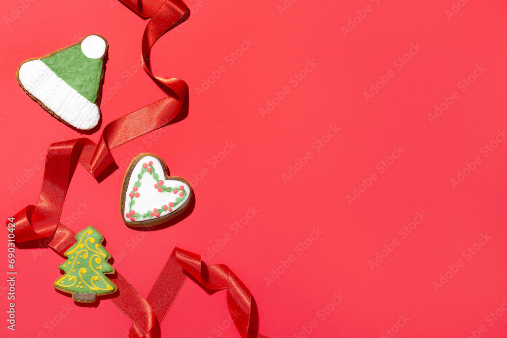 Delicious Christmas gingerbread cookies and a satin red ribbon on a red background. Top view. Space for text.