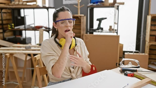 Handsome young hispanic female carpenter coughing in worry, battling cold or bronchitis at her carpentry studio - health care alert! photo