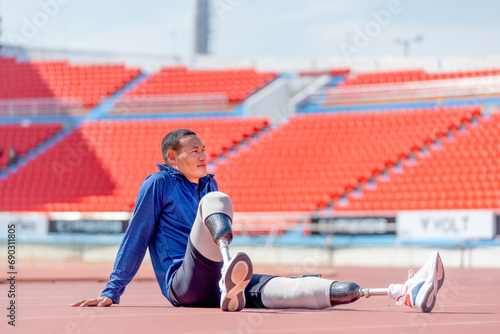 Sport man athlete with a prosthesis on his leg sit on the track and look forward to relax after exercise at the stadium. Sport concept.