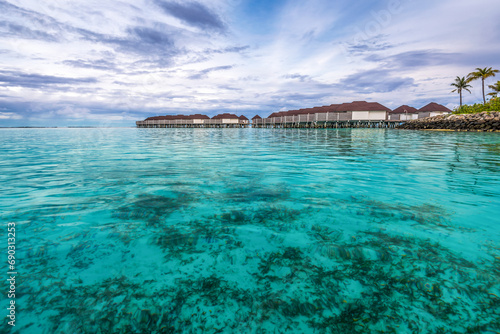 Scenic view of water villas in Maldives after sunset with turquoise pristine water and dramatic sky 