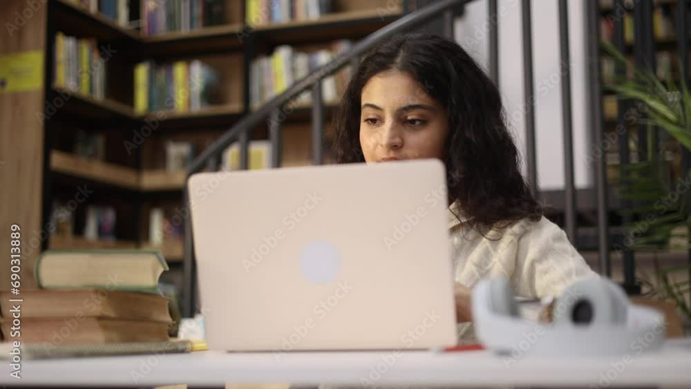 Charming confident curly girl preparing for exam at university studying and typing at library workplace Pretty student looking at laptop computer screen indoors Distance remote education