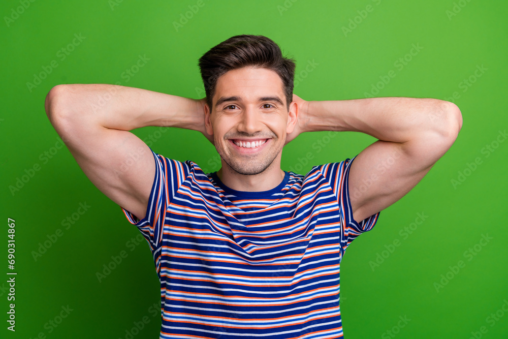 Photo of optimistic relaxed guy with stubble dressed striped t-shirt holding arms behind head chill isolated on green color background Photo of optimistic relaxed guy with stubble dressed striped t-shirt holding arms behind head chill isolated on green color background