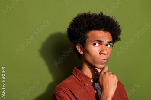 Photo portrait of handsome young guy touch chin look skeptical empty space dressed stylish brown outfit isolated on khaki color background