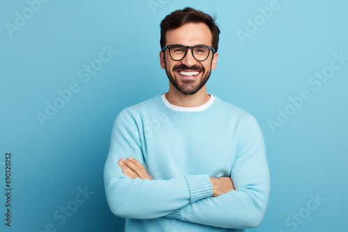 Young handsome man with beard wearing casual sweater and glasses over blue background happy face smiling with crossed arms looking at the camera. Positive person