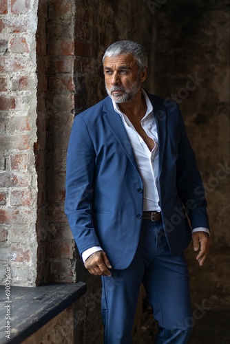 A handsome middle-aged man in a blue formal suit poses on a gray background. Portrait of a businessman. A handsome middle-aged man poses on a gray background with a place to copy