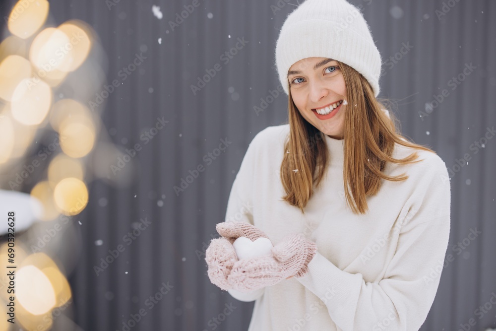 Happy woman in knitted mittens holding a snow heart on a winter snowy day Happy woman in knitted mittens holding a snow heart on a winter snowy day