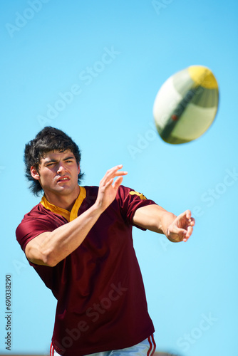 Sport, ball and male rugby player catching in training on a blue sky background. Professional athlete, uniform and confident fit exercise or workout for fitness game with a sportsman outdoors