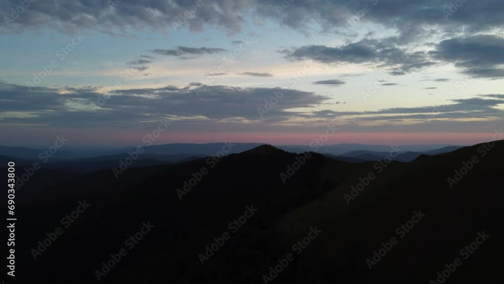 Static photography of mountains in the dark surrounded by bluish fog. Clouds line the sky with a slight pink tint from the recent sunset. Static photography of mountains in the dark surrounded by bluish fog. Clouds line the sky with a slight pink tint from the recent sunset.