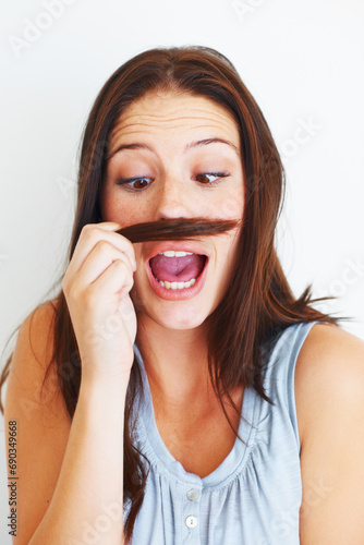Woman, silly and playing with hair mustache by white background, hairstyle and funny joke in studio. Female model person, comic and comedy for haircare or goofy, beauty treatment and cosmetology