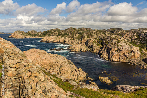 Rocky coast of Norway, mountains covered with moss and grass strong currents and dangerous cliffs. Cumulus clouds against a bright blue sky. Near Lindesnes Lighthouse, North Sea.