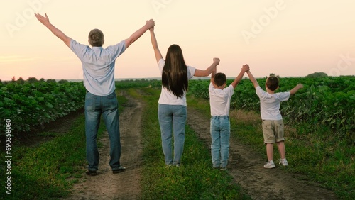 Joyful family with kids raises hands standing in meadow during summer break. Delighted family and kids relish being together in natural park on vocation. Children with family raise hands in unison