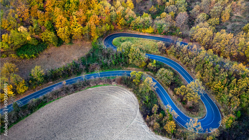 Italy, 08 December 2023 - aerial view of a hairpin road in the middle of a forest with autumn colors