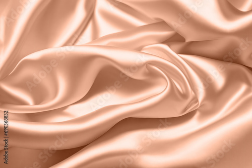 Abstract background, folds of silk fabric in peach fuzz color. © Ivan