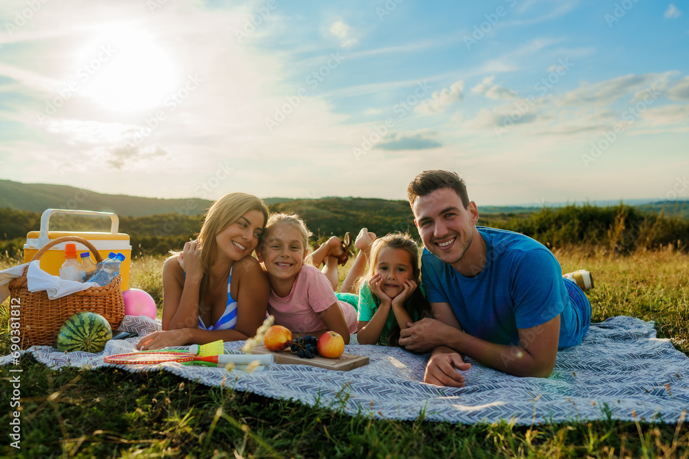 The family is lying on a blanket surrounded by fruit, having a picnic for the last day of summer vacation