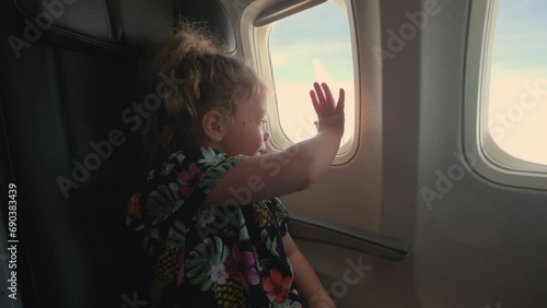A little girl sits in an airplane and looks on porthole photo