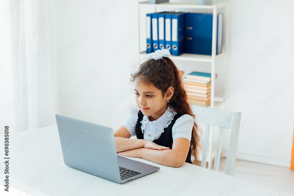 Little girl studying at desk with laptop online at school