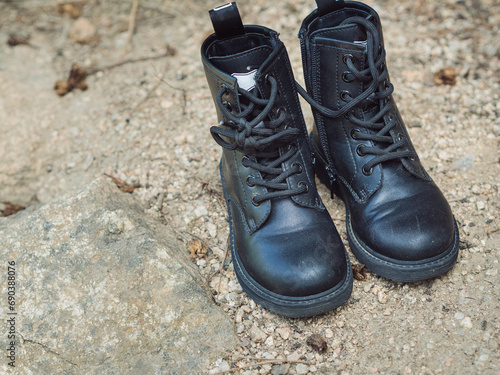 Horizontal straight from above close up of toddlers black leather boots on a rocky surface.