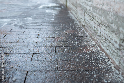 Deicing chemicals on pavement in winter. Salt grains on icy sidewalk, paving slab with rock salt in cold season. Slippery road sprinkled with technical salt and calcium. Prevent slipping concept photo