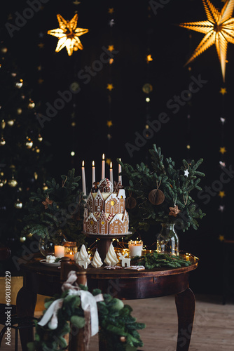 Christmas and New Year beautiful elegant family dinner table setting decorated with candles, fir tree branches, handmade craft toys. Gorgeous big homemade cake with gingerbread houses as centrepiece.