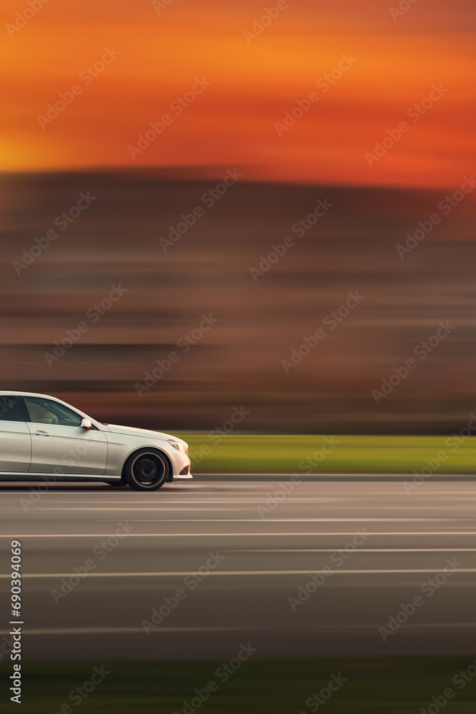 A fast moving car. Car with abstract speed blur background in evening with orange sky. Side view of the front of the car