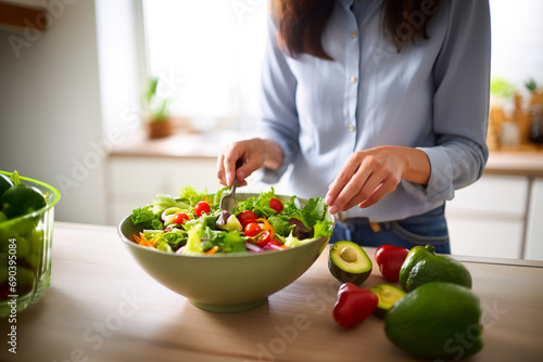 View of a woman's hands busy preparing salad in a bowl.