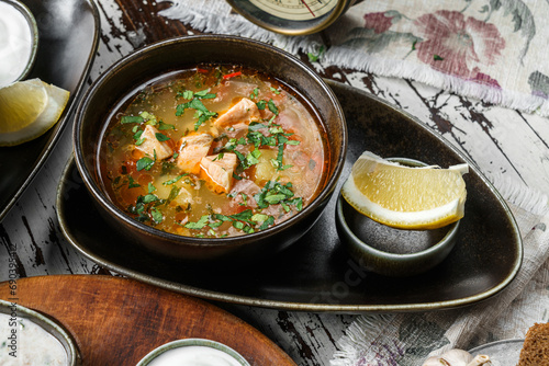 Foto Fish soup with salmon, greens and lemon on bowl on rustic wooden background