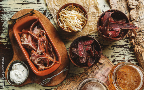 Smoked cured pork's ears, bacon, lard, dried squid, Sujuk, Basturma in bowl and two glasses of beer in wooden background. Beer snacks, party, top view, flat lay, toning photo