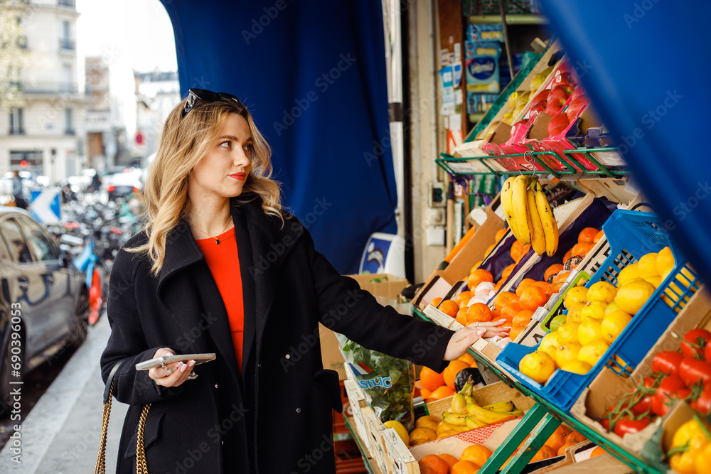 Stylish young woman in black coat buys fresh fruits at street market. Modern business women.