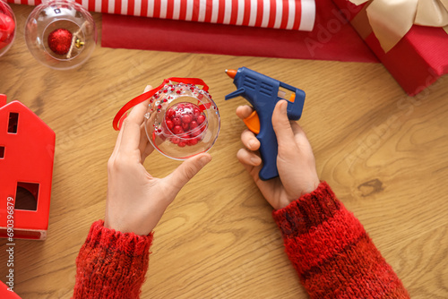 Woman holding glue gun and decorating Christmas ball with rhinestones on table