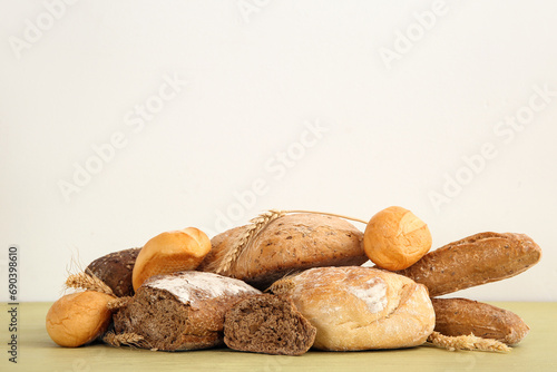 Loaves of different fresh bread with wheat spikelets on green wooden table