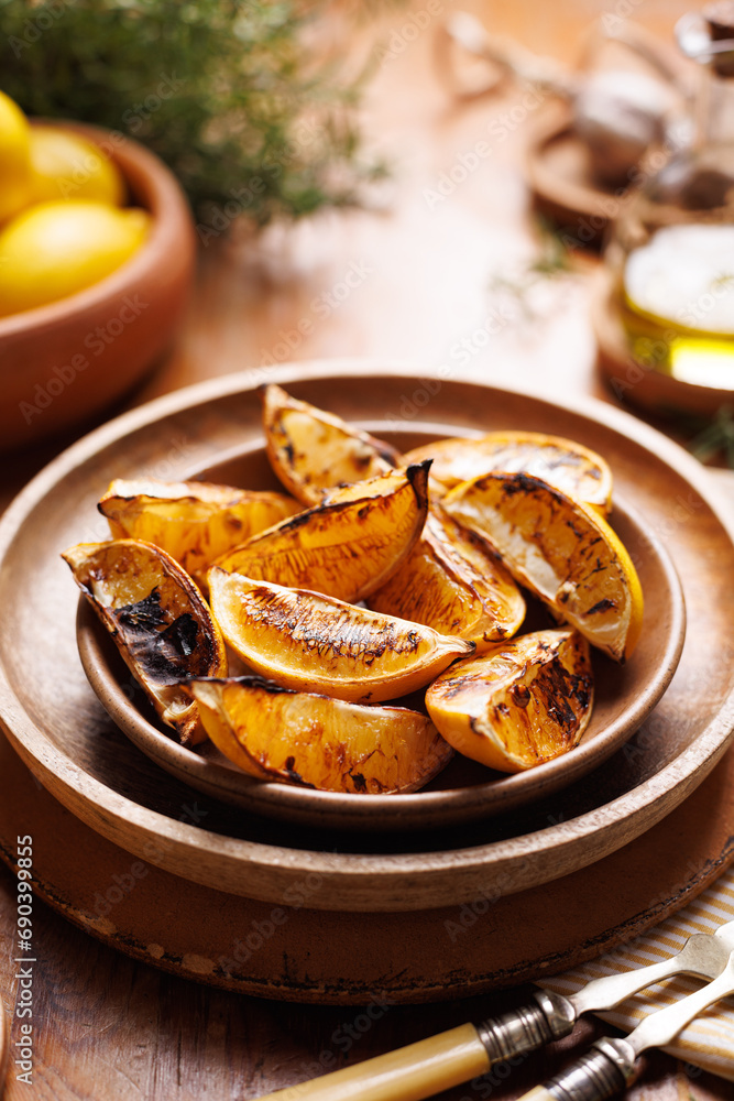 Grilled lemon pieces, wedges on a ceramic plate, close up view. Perfect addition to dishes and an ingredient of delicious lemonade made from grilled lemons Grilled lemon pieces, wedges on a ceramic plate, close up view. Perfect addition to dishes and an ingredient of delicious lemonade made from grilled lemons