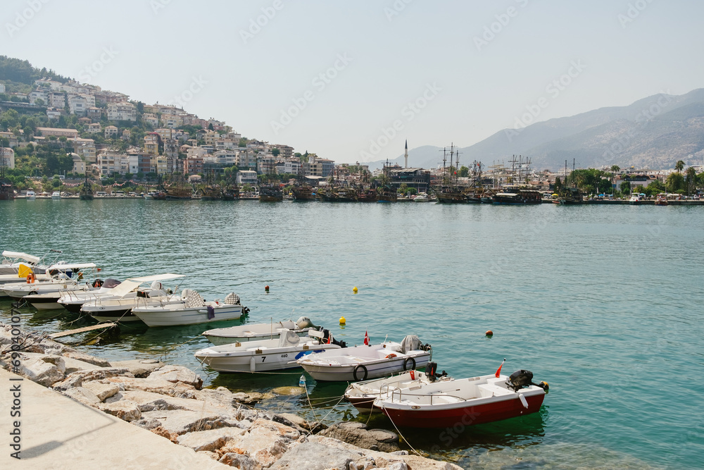 Idyllic seaside view of a Mediterranean town with boats moored in clear waters, against a backdrop of terraced houses and hills