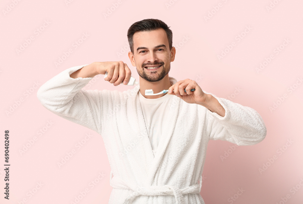 Handsome man squeezing tooth paste onto brush on pink background Handsome man squeezing tooth paste onto brush on pink background