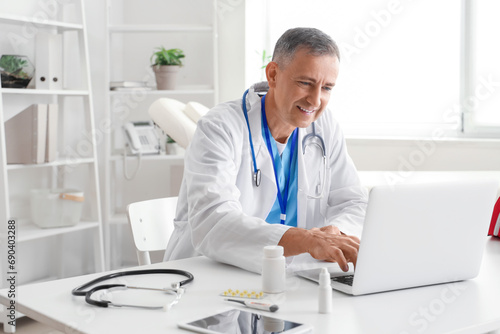 Mature doctor video chatting with patient on laptop at table in office