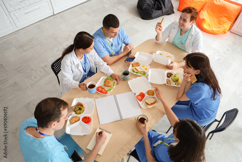 Team of doctors having lunch at table in hospital kitchen, top view photo