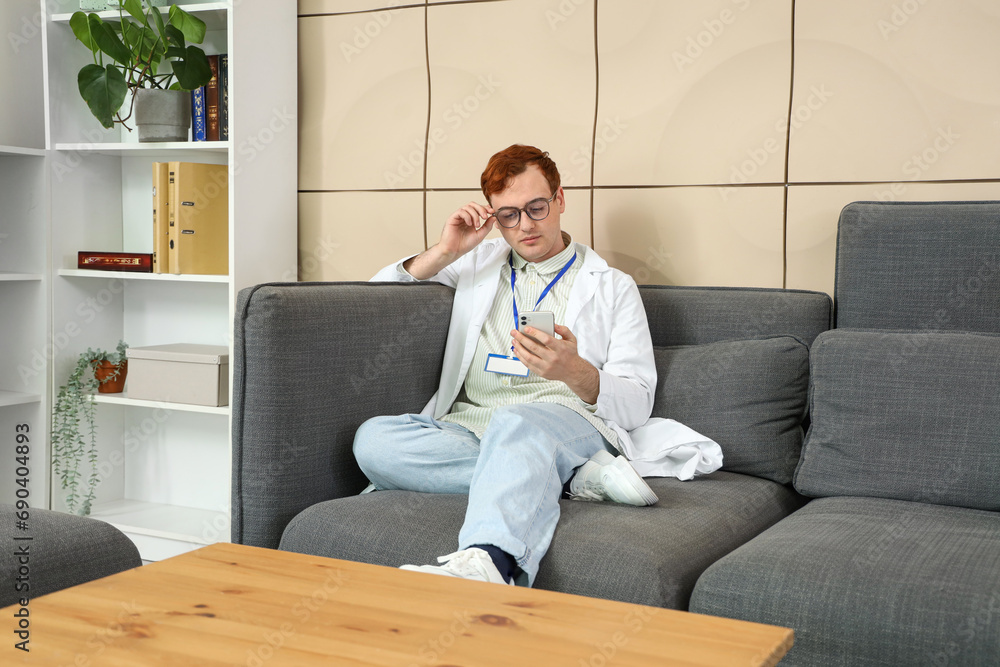 Male doctor using mobile phone on sofa in hospital lounge Male doctor using mobile phone on sofa in hospital lounge