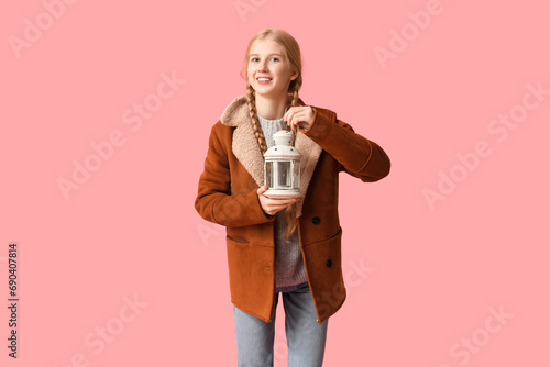 Beautiful young happy woman in warm winter clothes with lantern on pink background