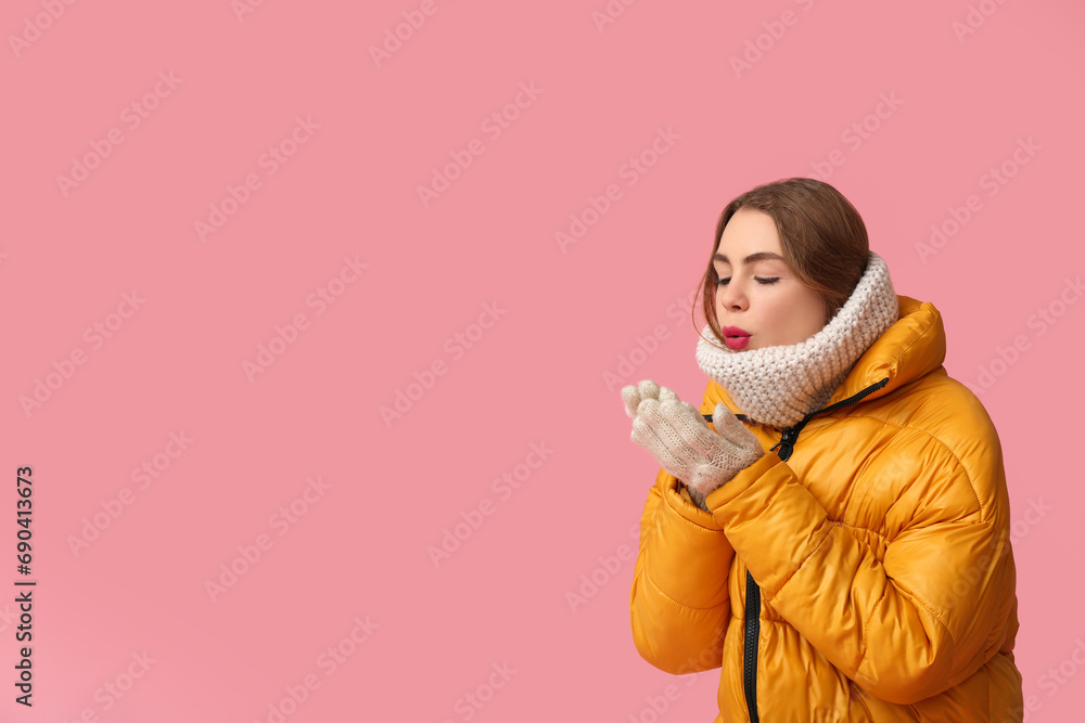 Frozen young woman in warm winter clothes warming hands on pink background Frozen young woman in warm winter clothes warming hands on pink background