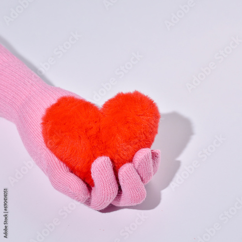 A woman's hand in a woolen glove holds a fur heart, the idea of love, giving, passion, kindness.