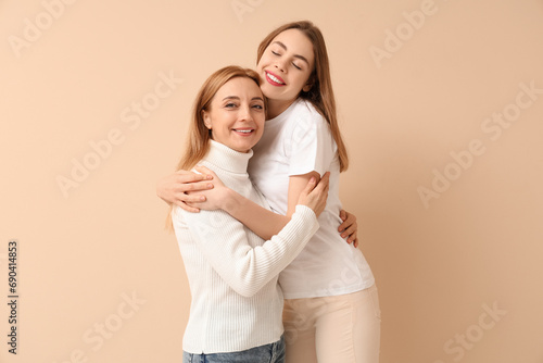 Beautiful young woman hugging her mother on beige background. International Hug Day